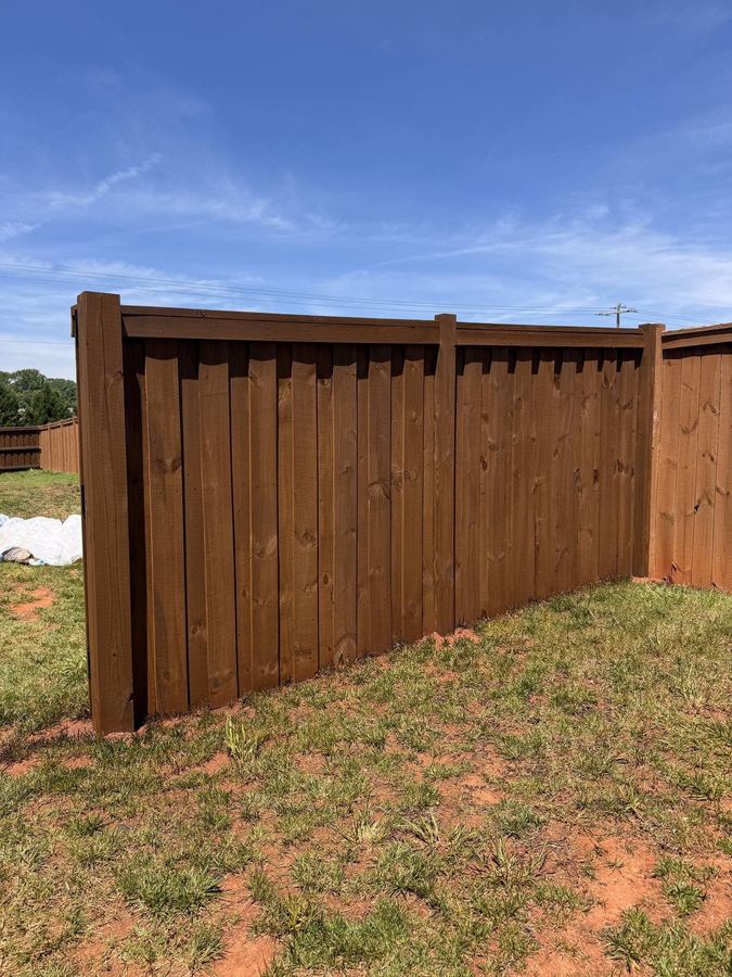 Freshly stained board-on-board fence corner under a blue sky