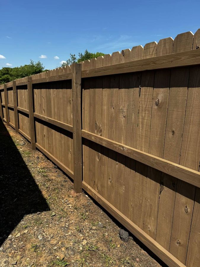 Long dark stained privacy fence running along a road beside the water