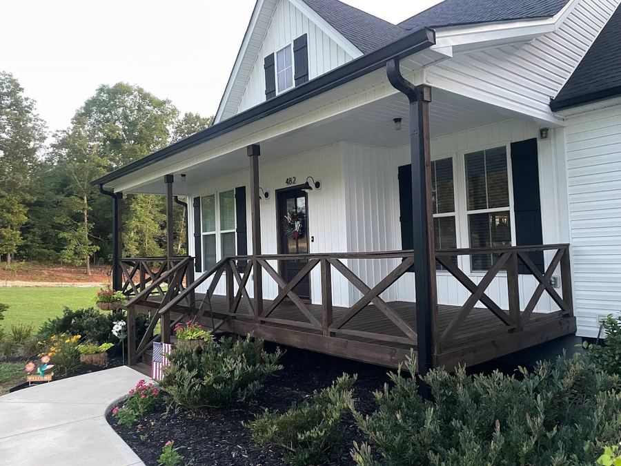 Covered front porch with dark stained posts and rails on a white farmhouse