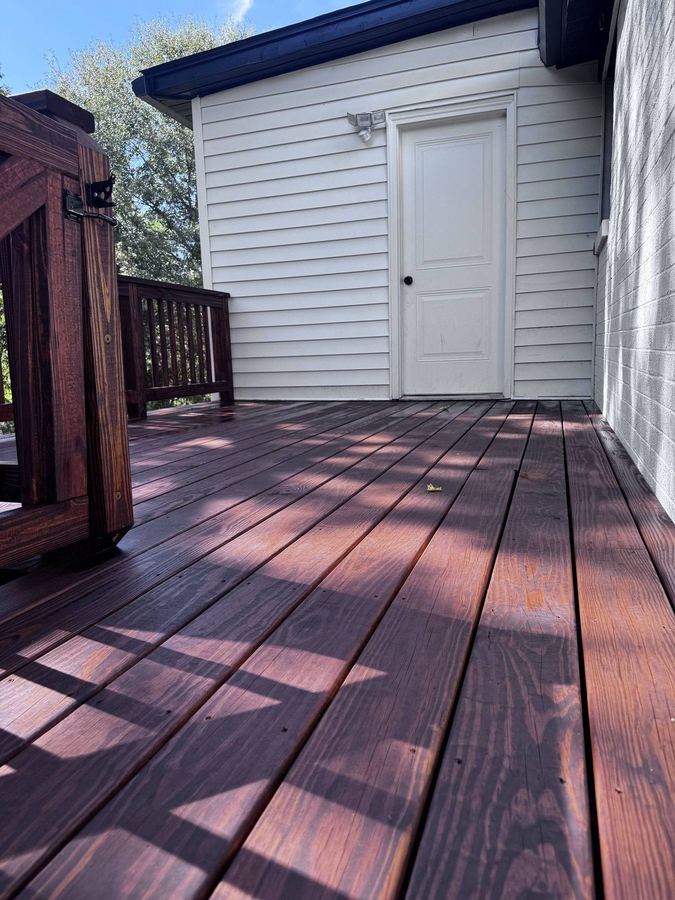 Deep red-brown deck boards in afternoon light beside a white house