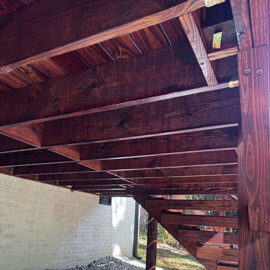 Underside of a stained deck showing joists and beams with a matching coat