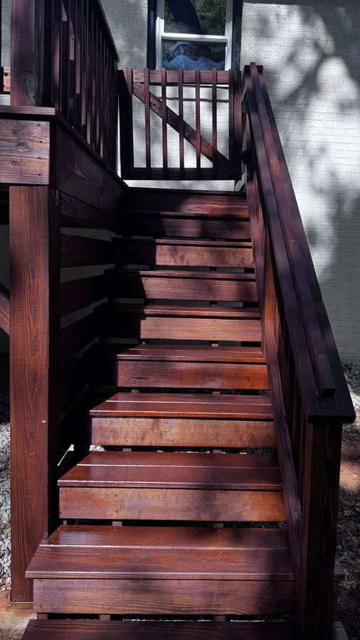 Dark stained deck stairs with a matching gate at the top against a brick wall