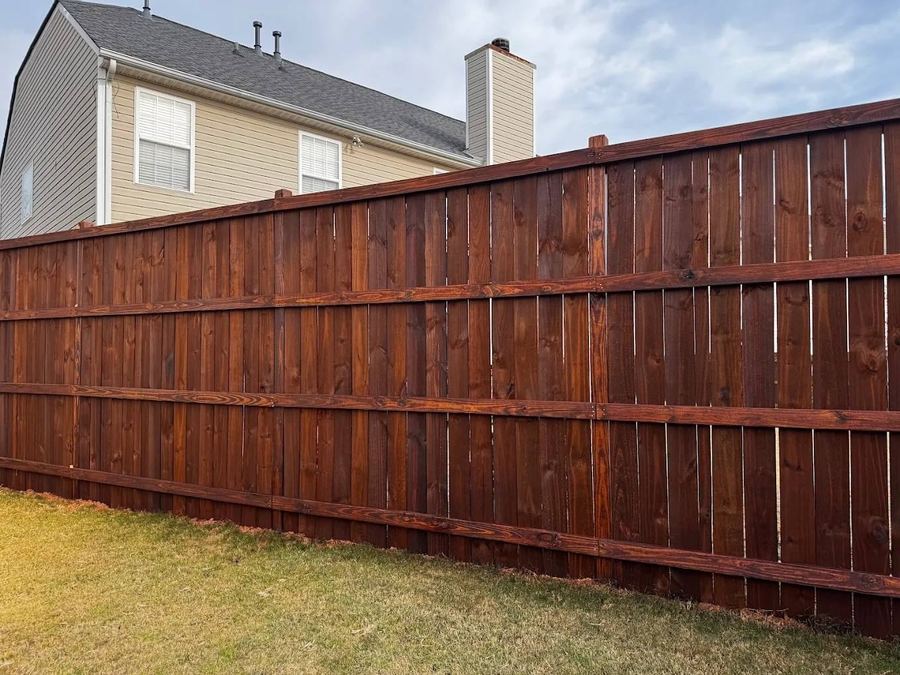 Eight-foot privacy fence with a fresh deep red-brown stain beside a two-story house