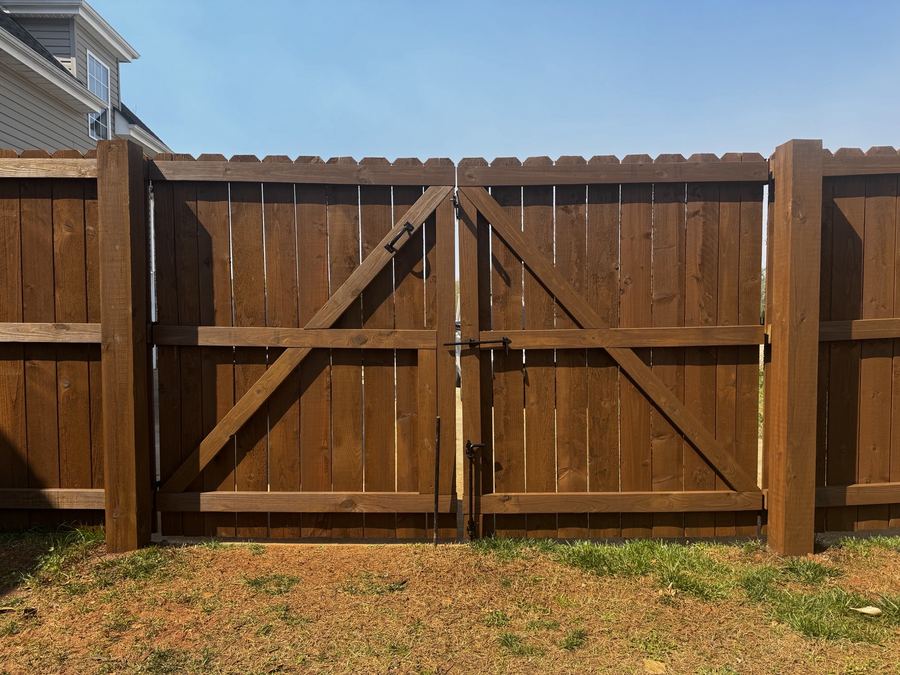 Wooden double gate with diagonal cross-bracing and black latch hardware between heavy posts