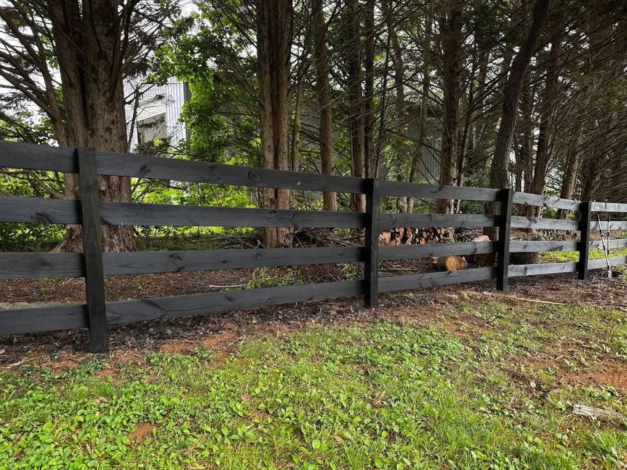 Four-board farm rail fence stained black along a tree line