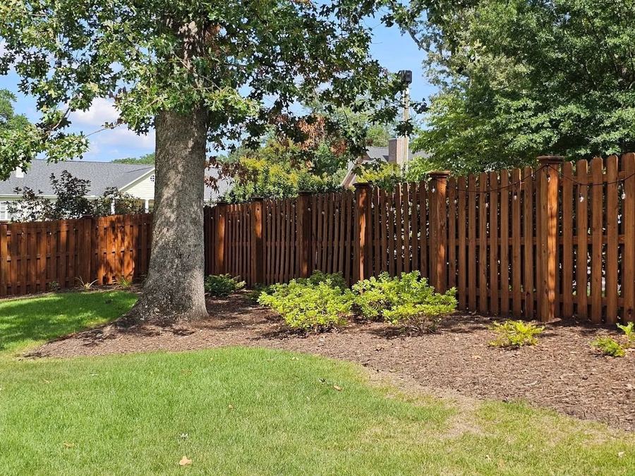 Dark stained privacy fence wrapping a backyard with a shade tree and mulched beds