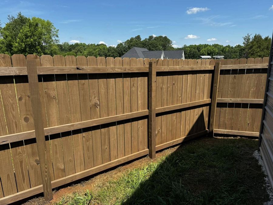 Interior face of a stained privacy fence showing posts and rails in sun