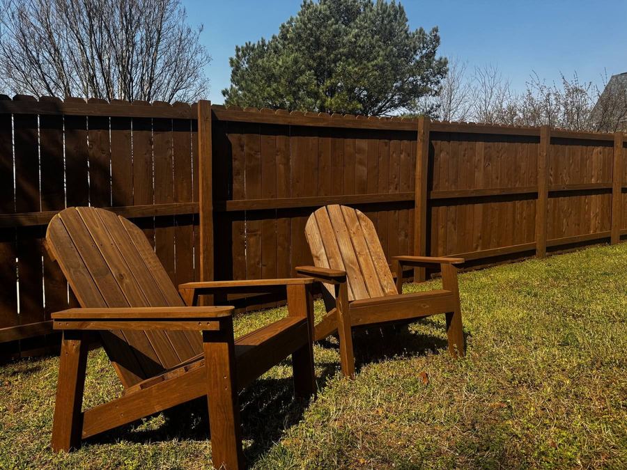 Stained privacy fence behind two matching wooden yard chairs on a lawn