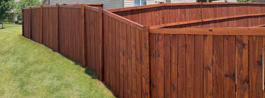 Long stained privacy fence running down a slope beside a house