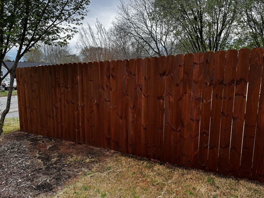 Dog-ear privacy fence with a warm dark stain under an overcast sky