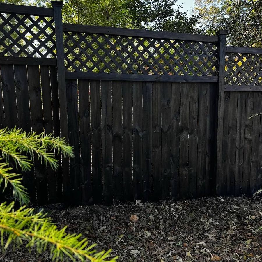 Lattice-top privacy fence stained near black behind green shrubs