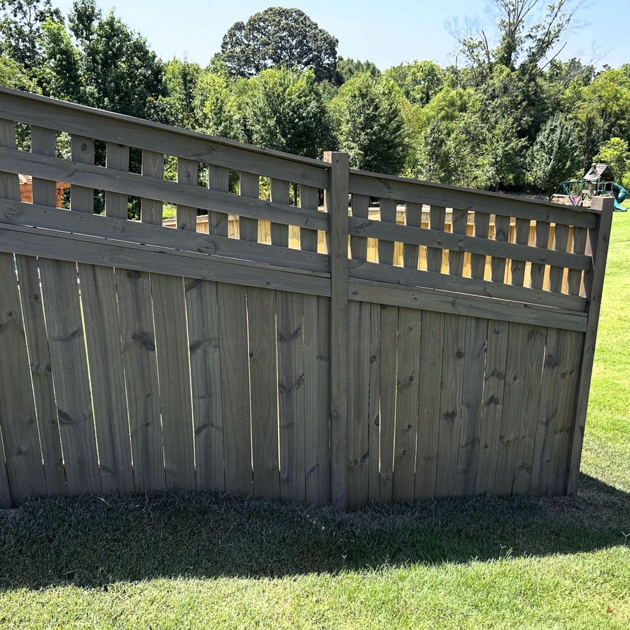 Lattice-top privacy fence stained grey on a sloped lawn