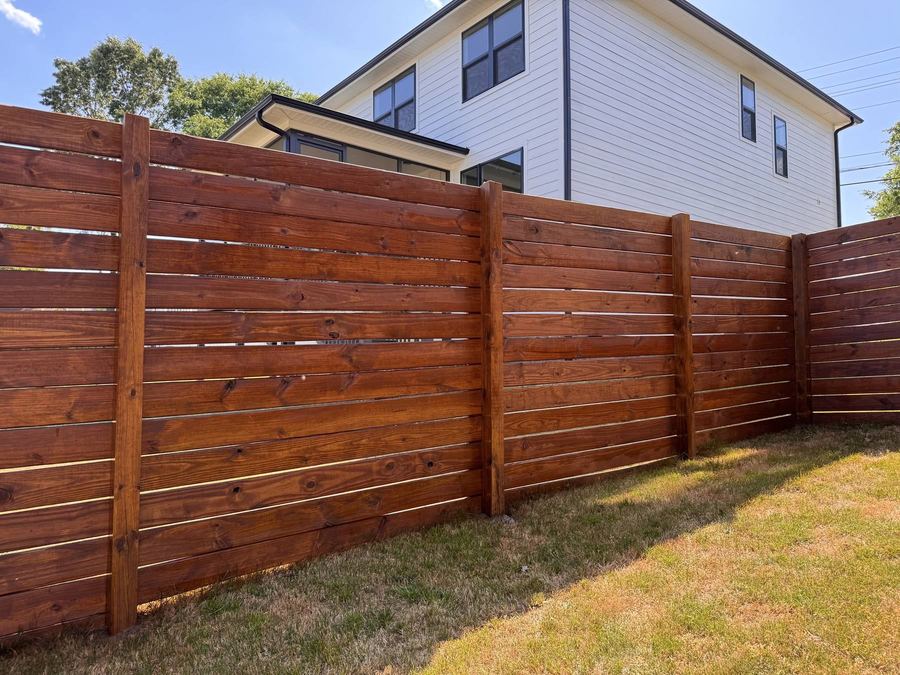 Horizontal board privacy fence with a warm stain in front of a white house