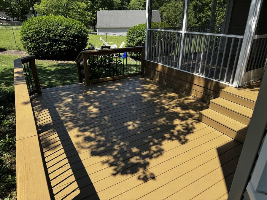 Deck floor with a solid stain and black metal rails beside a screened porch