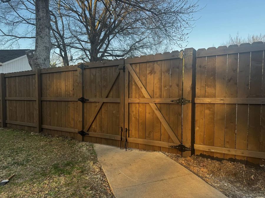 Stained privacy fence and gate with black hinges beside a concrete walk