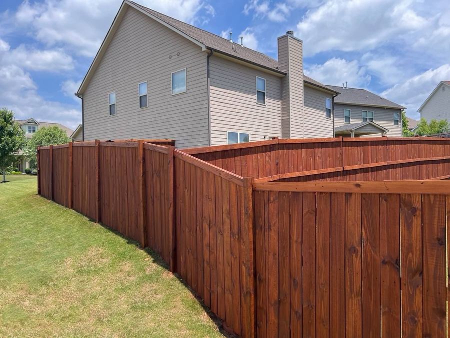 Stained privacy fence with a stepped corner beside a two-story house